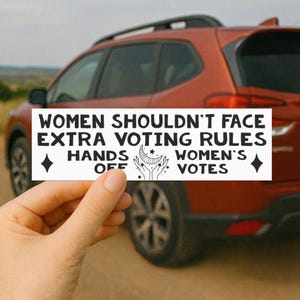 Peut inclure: Un autocollant blanc avec du texte noir qui dit "WOMEN SHOULDN'T FACE EXTRA VOTING RULES" et "HANDS OFF WOMEN'S VOTES." L'autocollant présente également un croissant de lune et un motif d'étoiles. L'autocollant est tenu devant une voiture rouge.
