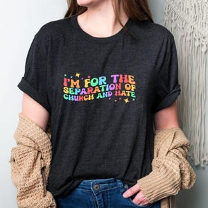 May include: A dark grey t-shirt with the text "I'm for the separation of church and hate" in rainbow colours.