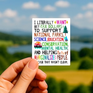 May include: A rectangular white sticker featuring multi-colored text that reads: I LITERALLY WANT MY TAX DOLLARS TO SUPPORT NATIONAL PARKS, SCIENCE, EDUCATION, CONSERVATION, MENTAL HEALTH, AND HELPING MARGINALIZED PEOPLE. IN CASE THAT WASN'T CLEAR.