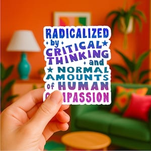 May include: A white sticker with the text "RADICALIZED by CRITICAL THINKING and NORMAL AMOUNTS of HUMAN COMPASSION" in blue, purple, and teal. The sticker is held in a hand against a colorful background.