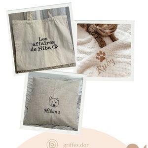 May include: A set of three personalised embroidered items for pets. A white tote bag with the text "Les affaires de Hiba" and a paw print, a white blanket with a brown paw print and the text "Ruby", and a beige pillow with a black silhouette of a dog and the text "Hibana".