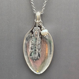 May include: A silver-toned spoon pendant necklace featuring an ornate handle design with the word Blessed stamped vertically. The pendant is suspended from a silver chain and accented with a single small white pearl bead attached to the top.