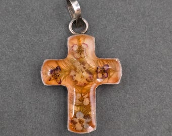 May include: A cross-shaped pendant featuring a clear resin body with embedded dried flowers in shades of orange, yellow, and purple. The pendant is encased in a silver-toned metal frame and includes a silver-toned metal bail at the top for hanging.
