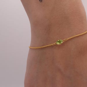 May include: A gold chain bracelet with a single green gemstone.