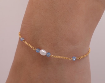 May include: A gold chain bracelet with a single white pearl and blue crystal beads.