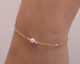 May include: A gold chain bracelet with a single white pearl and pink crystal beads.