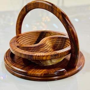 May include: A handcrafted wooden basket with a handle. The basket is made of dark brown wood and features a unique design with a round base and a curved handle. The basket is likely used for serving or displaying items.
