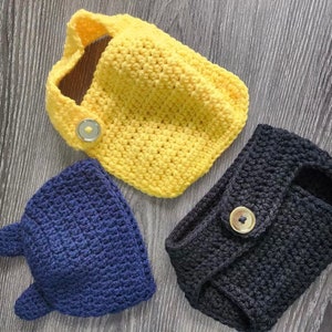 May include: Three crocheted hats in yellow, blue, and black with buttons. The hats are made with a textured stitch.