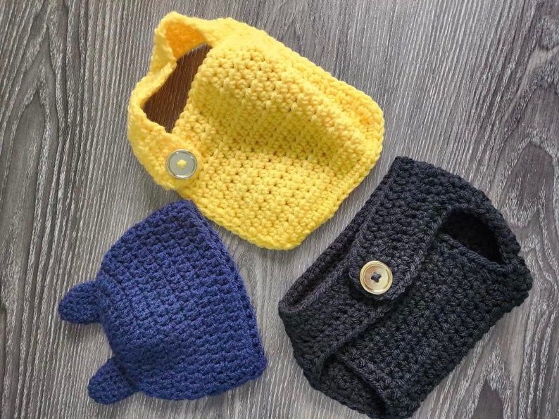 May include: Three crocheted hats in yellow, blue, and black with buttons. The hats are made with a textured stitch.