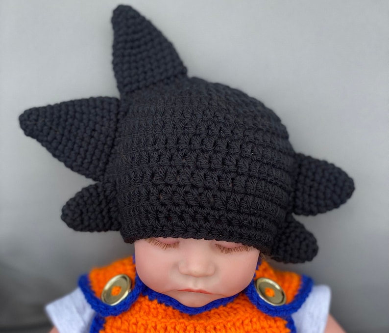 May include: A black crocheted hat with a spiky design, worn by a baby doll.