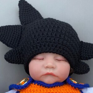 May include: A sleeping baby wearing a black crocheted hat with spiky points, resembling a popular anime character's hair. The baby is also wearing an orange and blue crocheted outfit.