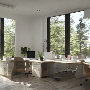 May include: Two white desks with wooden tops and drawers, facing each other in a modern office space. The desks are set up for two people, each with a chair, a computer monitor, and a lamp. The windows behind the desks offer a view of a lush green forest.