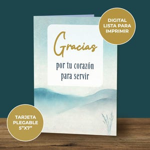 May include: A folded card with a watercolor background of blue and white hills. The card says "Gracias por tu coraz&oacute;n para servir" in gold lettering. The card is 5 inches by 7 inches.