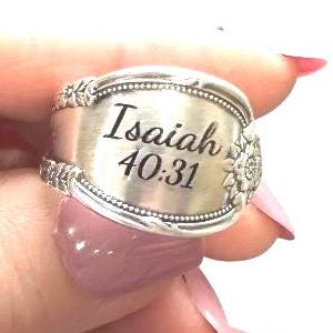 May include: A silver-toned metal ring crafted from a repurposed spoon handle. The center of the ring features the engraved text Isaiah 40:31 in a black script font, flanked by embossed floral details on the left and right sides of the band.