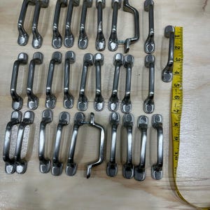 May include: A collection of 20 silver cabinet pulls or drawer pulls. The pulls are all different shapes and sizes, but they all have a similar style. They are all made of metal and have a brushed finish.