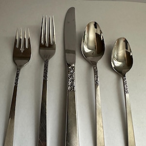 May include: A set of five silver-colored flatware pieces: two forks, a knife, and two spoons. The handles have a floral design. The knife blade is smooth, and the spoons have a rounded bowl shape.