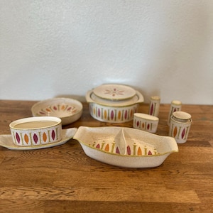 May include: A collection of vintage ceramic serving dishes with a speckled beige finish. The set includes a divided serving dish, covered casserole, bowls, and salt and pepper shakers. Each piece features a repeating pattern of colorful, stylized leaf shapes.