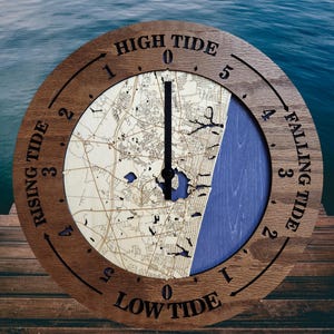 May include: A round wooden tide clock with a map design. The clock face features the words "High Tide," "Falling Tide," "Low Tide," and "Rising Tide." The clock hands point to the current tide level. The background is a blue water scene.
