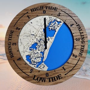 May include: A round wooden tide clock with a detailed map design. The clock face features a blue section representing the ocean and a map of the coastline. The clock has black hands and text that reads "HIGH TIDE" and "LOW TIDE".