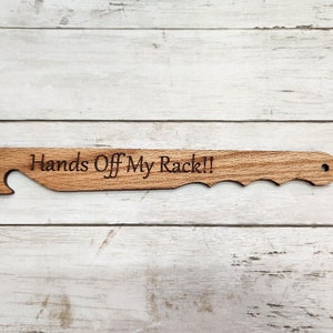 Może przedstawiać: Drewniane narzędzie z uchwytem i hakiem na jednym końcu. Narzędzie jest grawerowane tekstem "Hands Off My Rack!!".