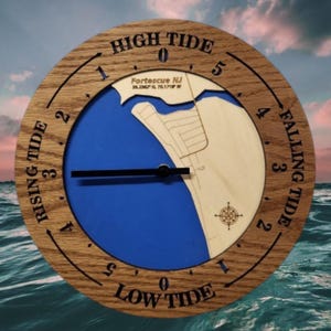 May include: A round wooden tide clock with a blue and beige face. The clock face features a map of Fortescue NJ, with text indicating high and low tide, and the time. The clock hands are black.