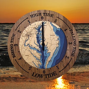 May include: A round wooden tide clock with a map of a coastal area. The clock face features a detailed map in shades of blue and tan, with the words "High Tide," "Falling Tide," "Low Tide," and "Rising Tide" around the perimeter.
