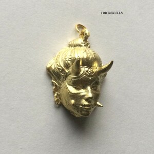 May include: Gold-colored pendant featuring a detailed, stylized face with horns and intricate hair. The pendant is a traditional Japanese design.