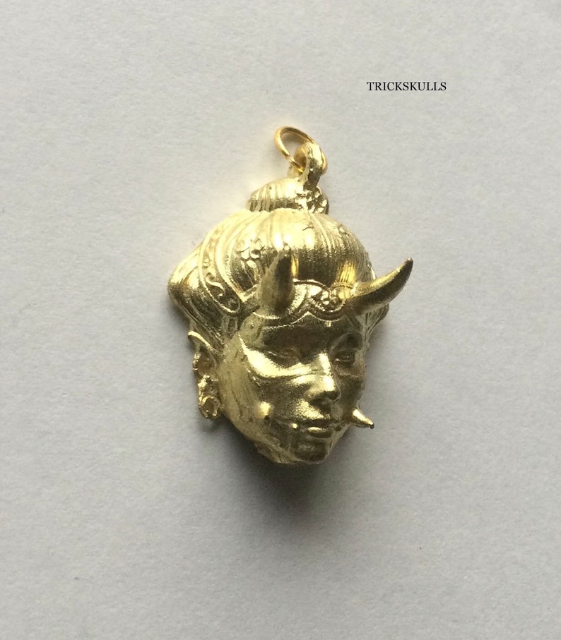 May include: Gold-colored pendant featuring a detailed, stylized face with horns and intricate hair. The pendant is a traditional Japanese design.