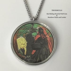 May include: A round pendant with a stainless steel chain. The pendant features a Red Riding Hood and wolf coin design. The coin depicts a woman in a red cloak and a yellow wolf in a forest setting. The text "TRICKSKULLS" is visible.