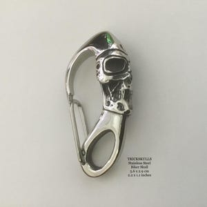 May include: A stainless steel biker skull carabiner clip. The skull is detailed with a helmet and facial features. The clip measures 2.2 x 1.1 inches. The design is from TRICKSKULLS.