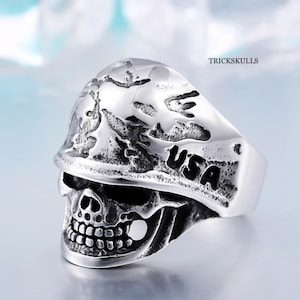 May include: A silver skull ring with a camouflage helmet design and the word "USA" engraved on the helmet.