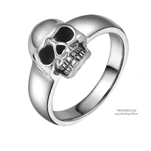 May include: A silver skull ring with black enamel eyes. The ring is made of 925 sterling silver. TRICKSKULLS is printed on the band.