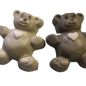 May include: Two small teddy bear shaped soaps, one is light brown and the other is white. Both have a pink heart on their chest.