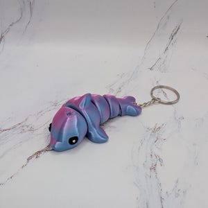 May include: A pink and blue dolphin keychain. The dolphin is made of plastic and has a silver key ring.