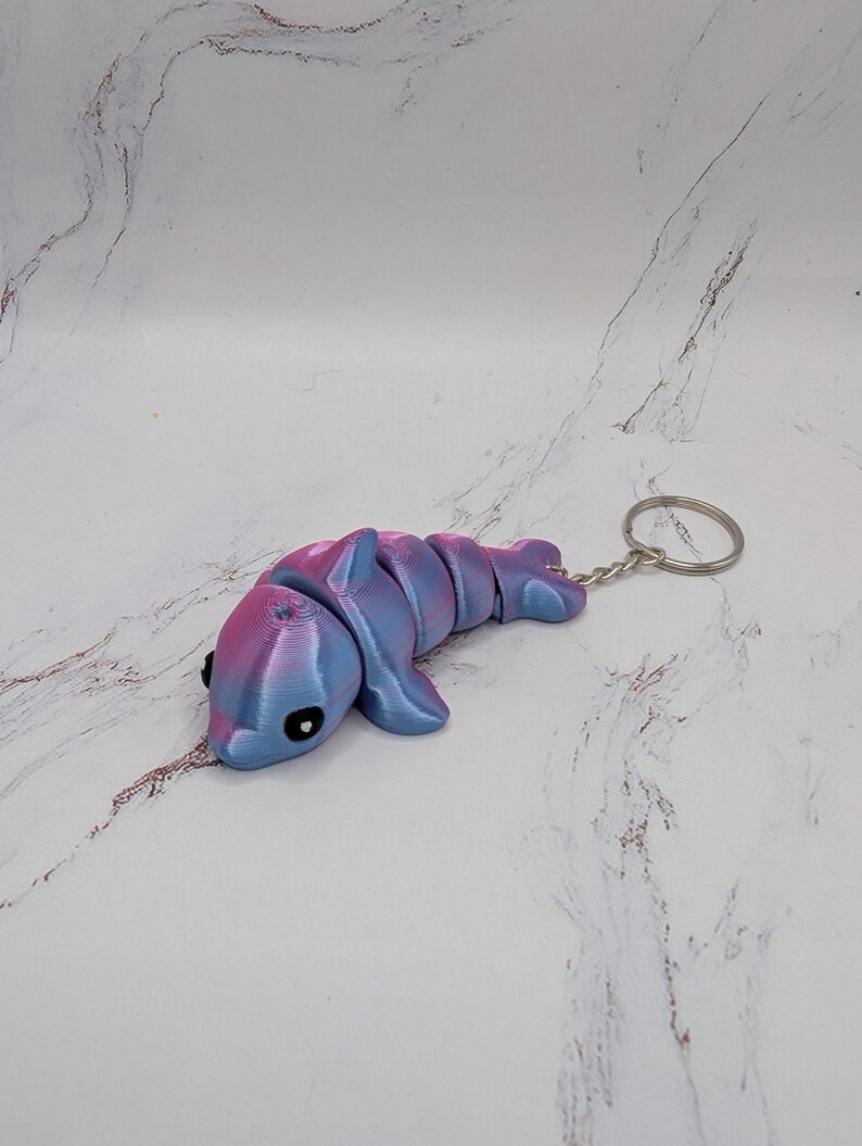 May include: A pink and blue dolphin keychain. The dolphin is made of plastic and has a silver key ring.