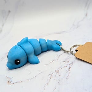 May include: A blue glow-in-the-dark dolphin keychain. The dolphin is made of a soft, pliable material and has a cute, cartoonish appearance.