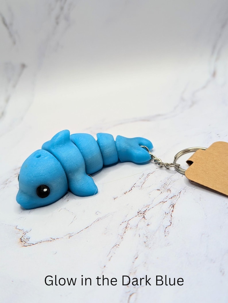 May include: A blue glow-in-the-dark dolphin keychain. The dolphin is made of a soft, pliable material and has a cute, cartoonish appearance.