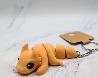 Pode incluir: Um chaveiro de cor pêssego com a forma de uma criatura de desenho animado com olhos pretos. O chaveiro está preso a uma corrente prateada e uma etiqueta marrom com um furo no centro. O texto "Sherbet" está impresso abaixo do chaveiro.