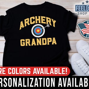 May include: Black t-shirt with the text "Archery Grandpa" in yellow letters. A target with red, blue, yellow, and white colors is in the center of the text. A white arrow is pointing to the target.