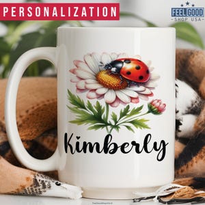 May include: White ceramic mug with a daisy and ladybug design. The mug has the name "Kimberly" printed on it in black.
