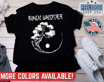 May include: Black t-shirt with white text that reads "Bonsai Whisperer" and a white silhouette of a bonsai tree with a yin yang symbol in the background.