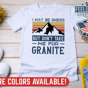May include: White t-shirt with a vintage mountain graphic and the text "I may be gneiss but don't take me for granite".