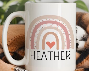 May include: White ceramic mug featuring a rainbow design in shades of pink, beige, and brown, with a heart at the center. The name "HEATHER" is printed in black below the rainbow. The mug has a curved handle and the word "PERSONALIZATION" is printed at the top.