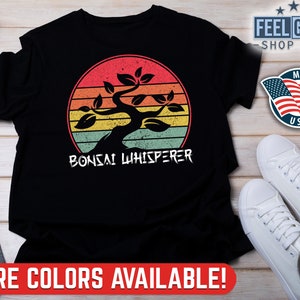 May include: Black t-shirt featuring a vintage-style sunset graphic with a bonsai tree. The text "Bonsai Whisperer" is printed below the graphic.