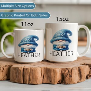 May include: Two white ceramic mugs with a blue gnome graphic and the name 'HEATHER' printed on them. The mugs are sitting on a wooden surface. The mugs are available in two sizes: 11 oz and 15 oz.