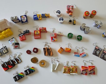May include: A collection of miniature food and household items turned into earrings. The earrings are made from various materials, including metal, plastic, and cardboard. Some of the items include cereal boxes, cans of food, and a cassette tape.