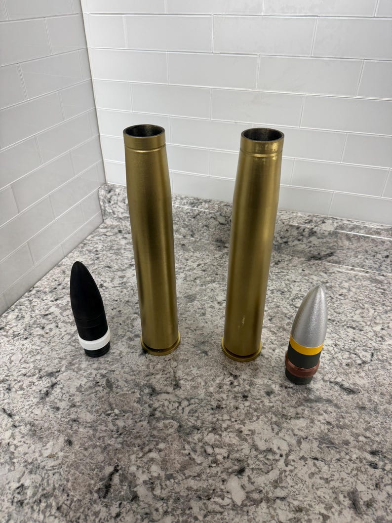 May include: Two gold-coloured metal cylinders and two bullet-shaped objects. One bullet is black with a white band, and the other is silver with a yellow band.