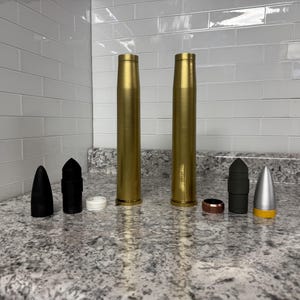 May include: A collection of gold, black and silver bullet casings. The casings are arranged in a row on a grey countertop.