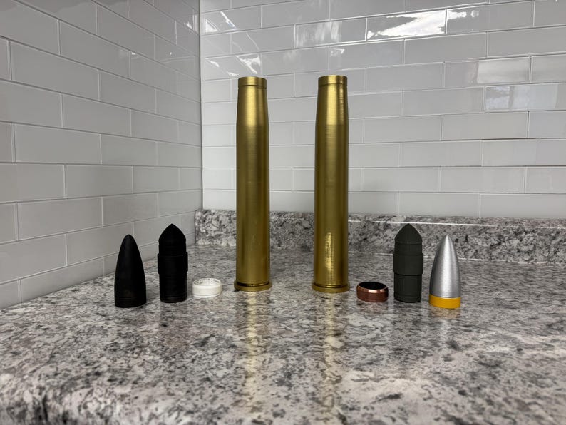 May include: A collection of gold, black and silver bullet casings. The casings are arranged in a row on a grey countertop.