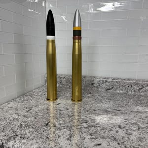 May include: Two gold-coloured artillery shells, one with a black tip and the other with a silver tip and yellow and brown bands.